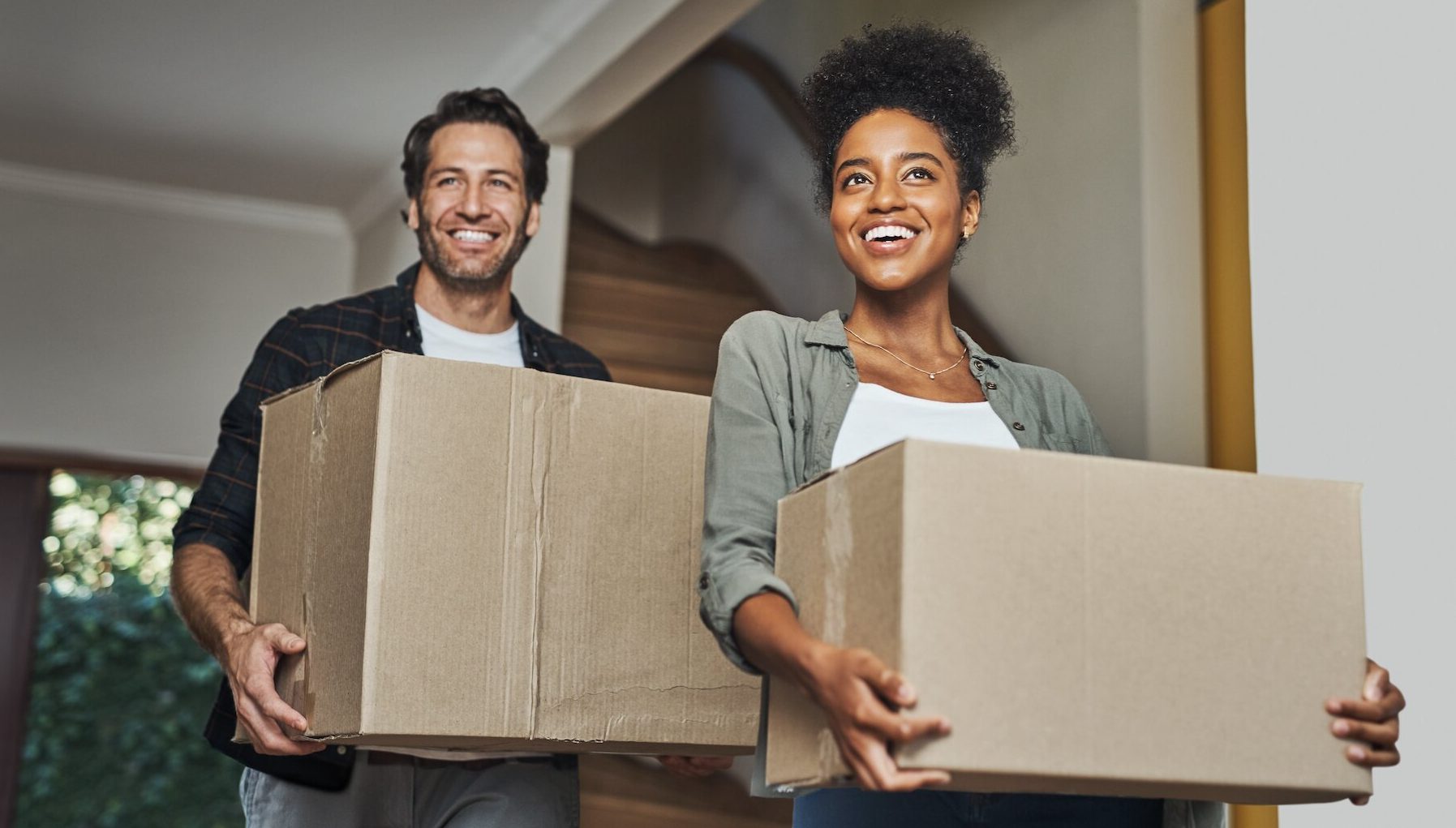 A photo of a couple moving into their new home holding cardboard boxes.